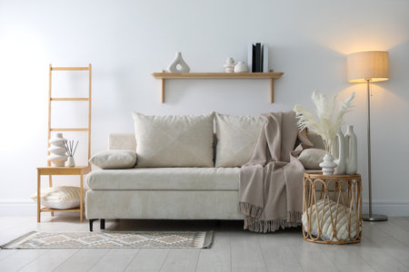 Comfortable sofa with pillows, blanket, lamp and different decor in room. Interior designの写真素材