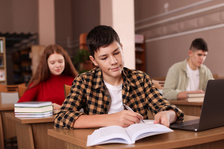 Boy taking notes at desk in libraryの写真素材