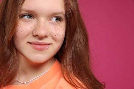 Beautiful teenage girl with freckles on pink background, closeup. Space for textの写真素材