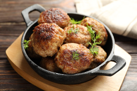 Tasty patties and dill in frying pan on wooden table, closeup