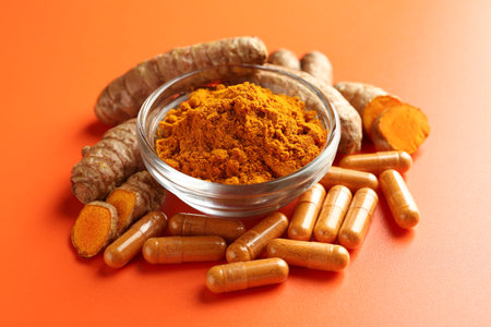 Turmeric powder in bowl, roots and capsules on orange background, closeupの写真素材