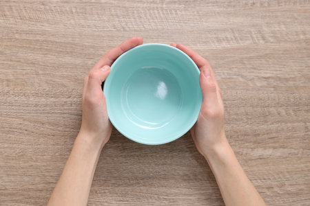 Woman holding empty bowl at wooden table, top viewの写真素材