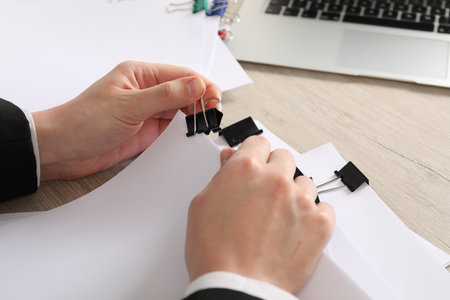 Woman attaching sheets of paper with metal binder clip at wooden table, closeupの写真素材