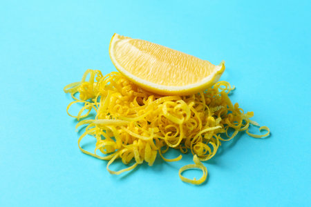 Lemon zest and piece of fresh fruit on light blue background, closeupの写真素材