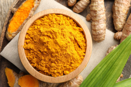 Turmeric powder in bowl, roots and leaves on table, flat layの写真素材