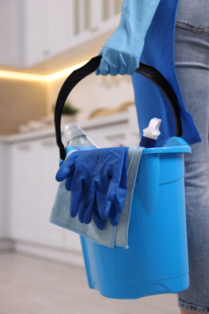Woman holding bucket with cleaning supplies in kitchen, closeupの写真素材