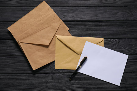 Kraft paper envelopes with letter and pen on black wooden background, flat lay. Mockup for designの写真素材