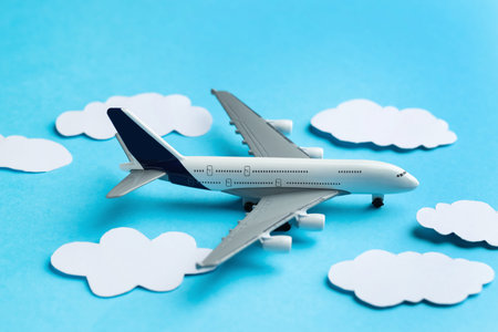 Plane model among paper clouds on light blue background, closeup