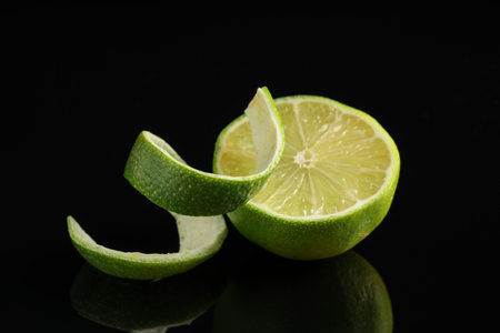 Fresh lime peel and half of fruit on black glass surface, closeupの写真素材