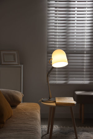 Stylish night lamp and book on side table near sofa in room. Interior design
