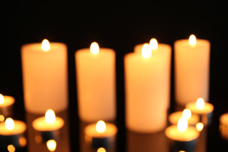 Blurred view of burning candles on mirror surface against black background, closeupの写真素材