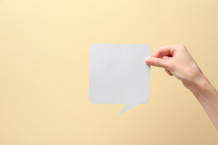 Woman holding blank speech bubble on beige background, closeup. Space for text