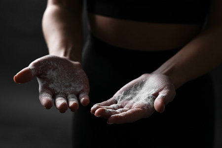 Woman with powder on her hands before training against black background, closeupの写真素材
