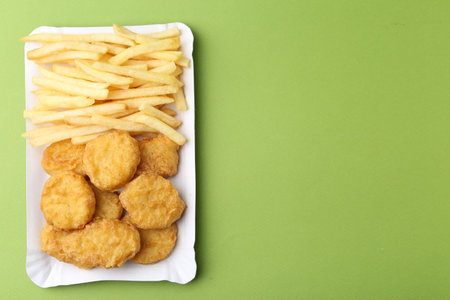 Tasty chicken nuggets and french fries on green background, top view. Space for text