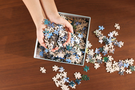Girl with box of puzzle pieces at wooden table, top viewの写真素材