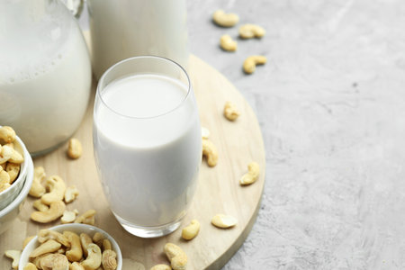 Fresh cashew milk in glass and nuts on grey table, closeup. Space for textの写真素材