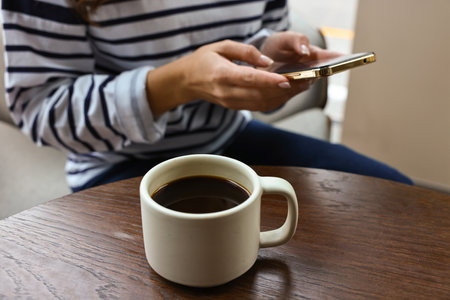 Woman with smartphone having coffee break at wooden table in cafe, closeupの写真素材