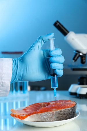GMO concept. Scientist injecting something into piece of salmon at table in laboratory, closeupの写真素材