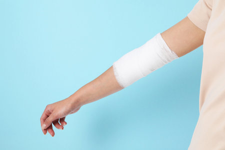 Woman with medical bandage on elbow against light blue background, closeup. Space for textの写真素材