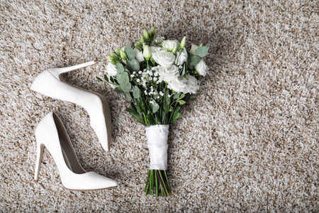 Wedding bouquet of beautiful flowers and bridal shoes on beige carpet, top view. Space for textの写真素材