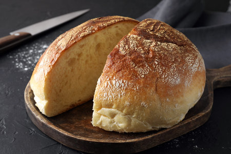 Cut loaf of bread on black table, closeup