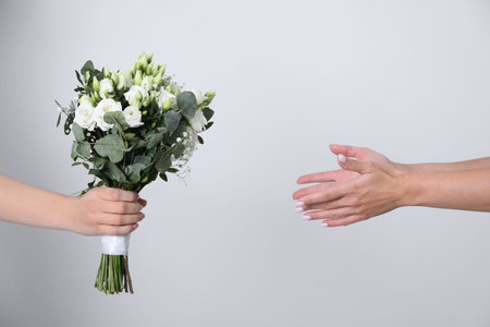 Bridesmaid giving beautiful wedding bouquet to bride on light background, closeupの写真素材