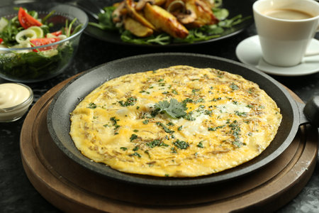 Tasty brunch. Delicious omelette, salad, fried potatoes and coffee served on black textured table, closeupの写真素材
