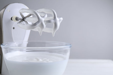 Hand mixer with whisks and bowl of whipped cream on white table, closeup. Space for textの写真素材