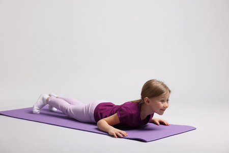Cute little girl exercising on fitness mat against light grey backgroundの写真素材