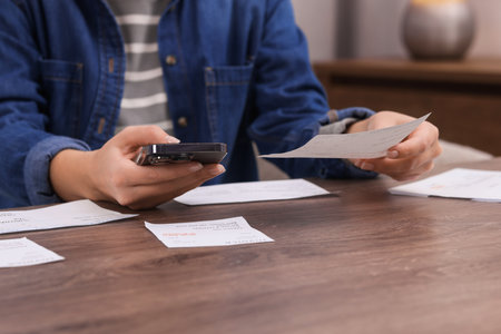 Paying bills. Woman with different invoices and phone at wooden table indoors, closeupの写真素材