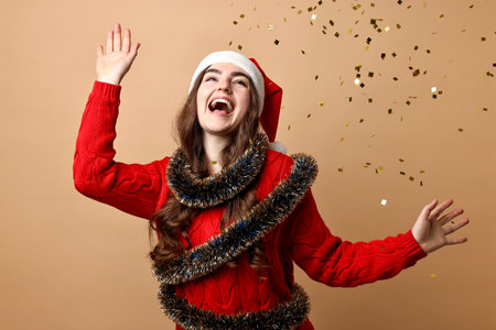 Happy young woman with tinsel under falling confetti on beige backgroundの写真素材