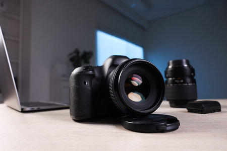 Professional photo camera, lens and laptop on wooden desk indoors, selective focus