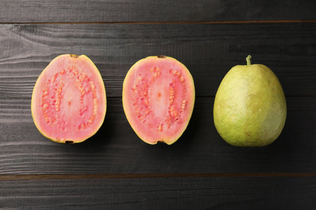 Fresh whole and cut guava fruits on black wooden table, flat layの写真素材