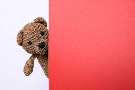 Cute knitted bear peeking out from red card on white background, space for textの写真素材