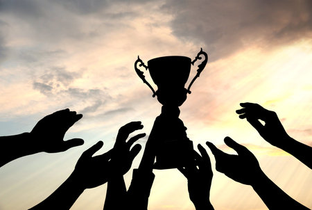Silhouettes of people reaching for trophy against sky, closeupの写真素材