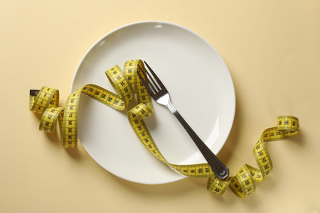 Bulimia. Plate with fork and measuring tape on beige background, top viewの写真素材
