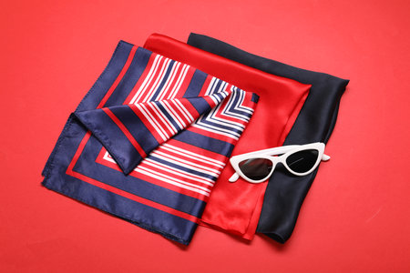 Stylish handkerchiefs and sunglasses on red background, top viewの写真素材