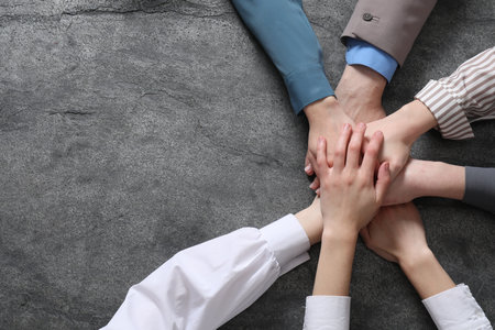 Business concept. Group of people stacking hands at grey textured table, top view. Space for textの写真素材