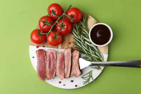 Delicious sliced beef tenderloin with different degrees of doneness, tomatoes, sauce and spices on green table, top viewの写真素材