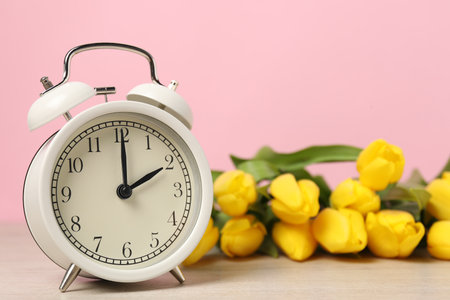 Spring time. Alarm clock and beautiful tulips on wooden table against pink backgroundの写真素材