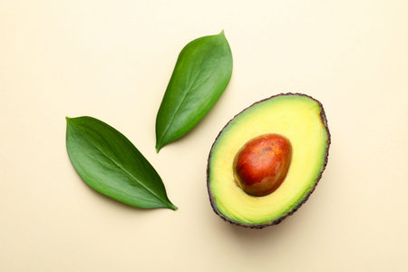 One cut ripe avocado and leaves on beige background, top view