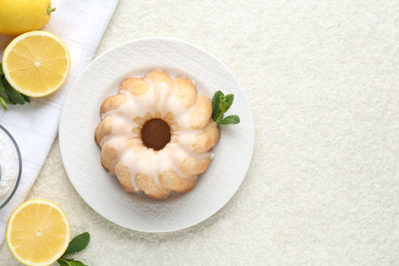 Delicious lemon cake with glaze, mint and citrus fruits on light textured table, flat lay. Space for textの写真素材