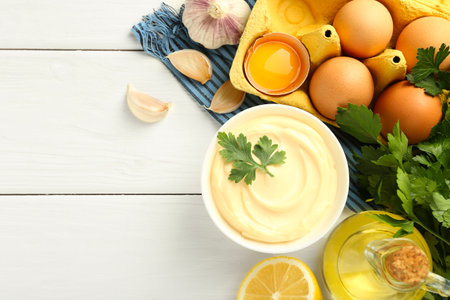 Delicious mayonnaise sauce with parsley in bowl and ingredients on white wooden table, flat lay. Space for textの写真素材
