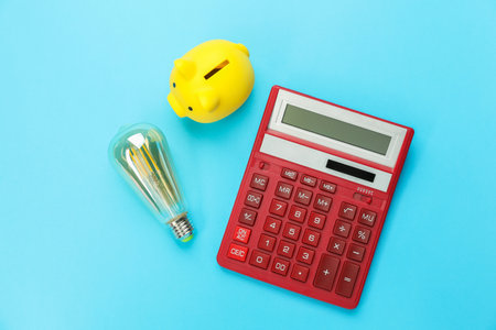 Piggy bank, calculator and lightbulb on light blue background, flat lay. Energy saving conceptの写真素材