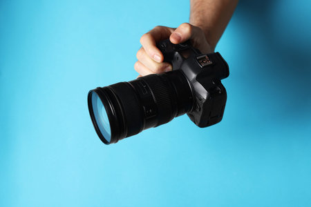 Photographer with professional camera on light blue background, closeup