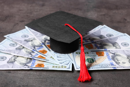 Graduate hat and dollars on gray textured table. Tuition paymentの写真素材