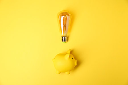 Light bulb and piggy bank on yellow background, flat lay. Energy saving conceptの写真素材