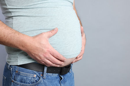 Overweight man in tight t-shirt on grey background, closeup. Space for textの写真素材