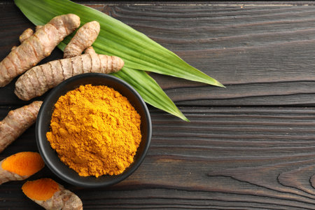 Aromatic turmeric powder in bowl, fresh roots and leaves on wooden table, flat lay. Space for textの写真素材
