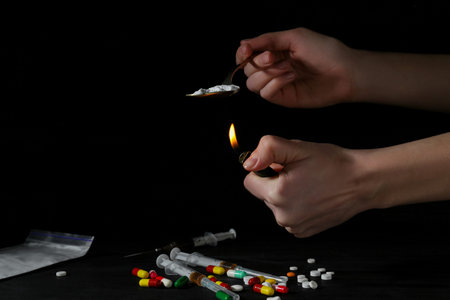 Drug addiction. Woman lighting spoon with powder against dark background, closeup. Space for text